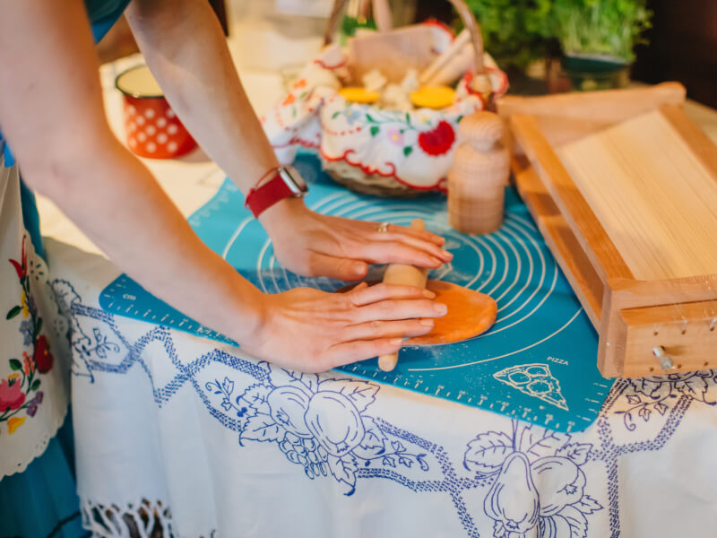 Woman rolling out orange pasta dough on a bench
